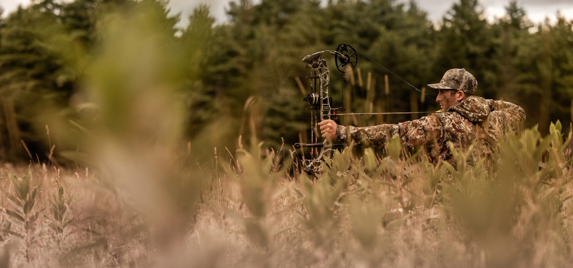 A hunter in a field with his bow drawn, taking aim