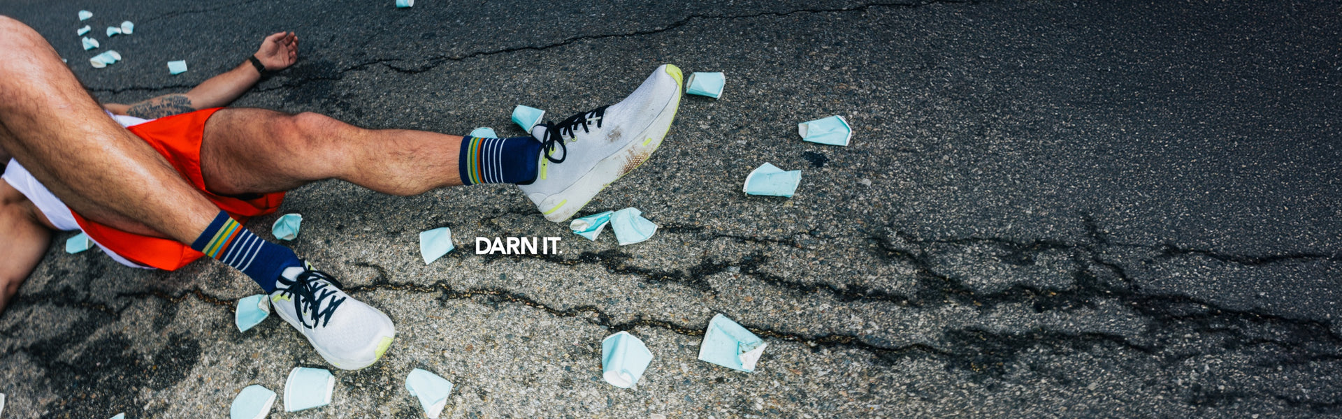 A marathon runner wearing Darn Tough run socks; he's collapsed on the ground with water cups all around him.