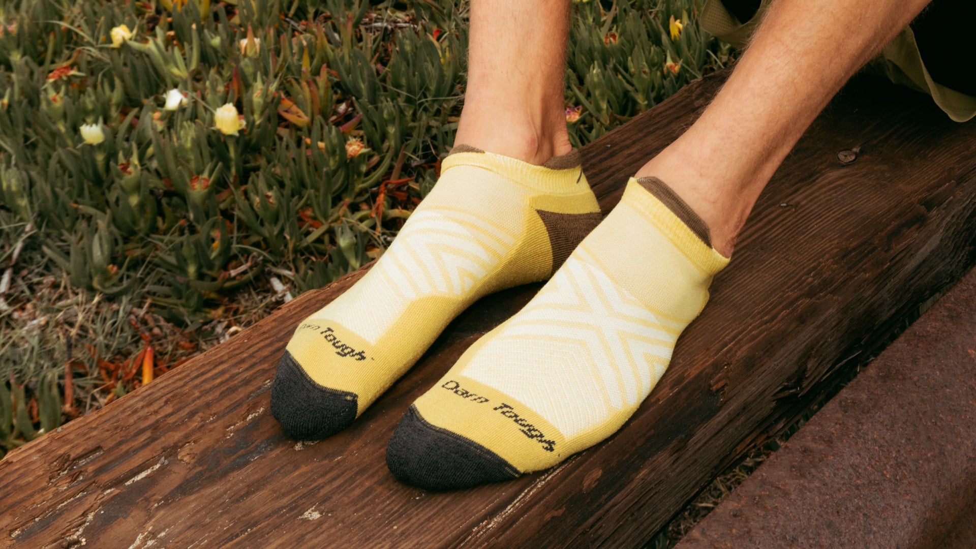 Models feet up on log wearing the no show running sock in sandstone