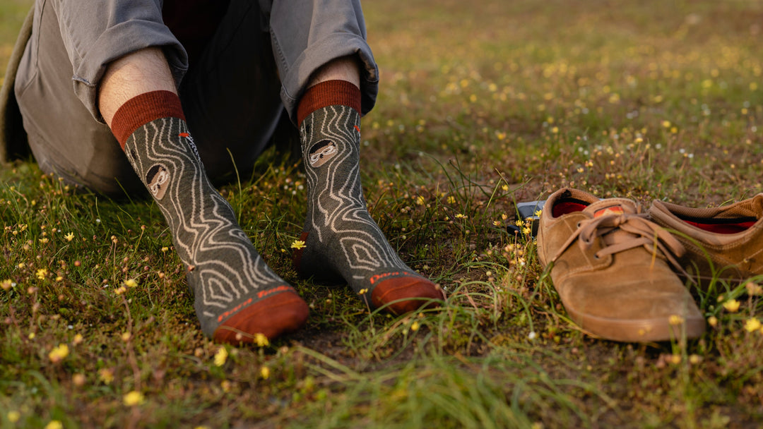 Models feet in grass field next to dress shoes wearing the woody Crew sock
