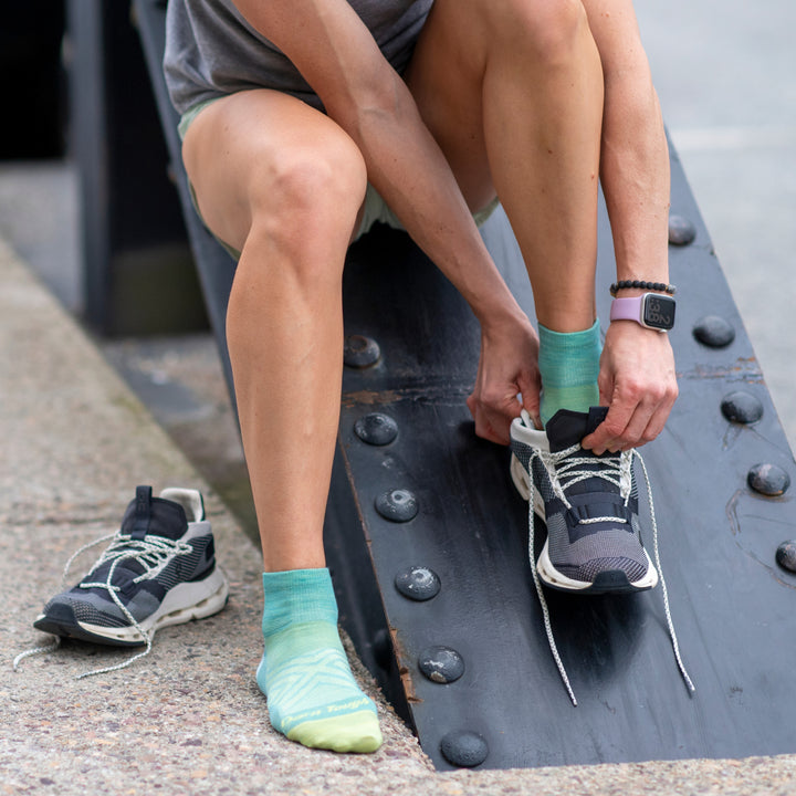 Runner pulling on running shoes over aqua blue quarter running socks knit from merino wool