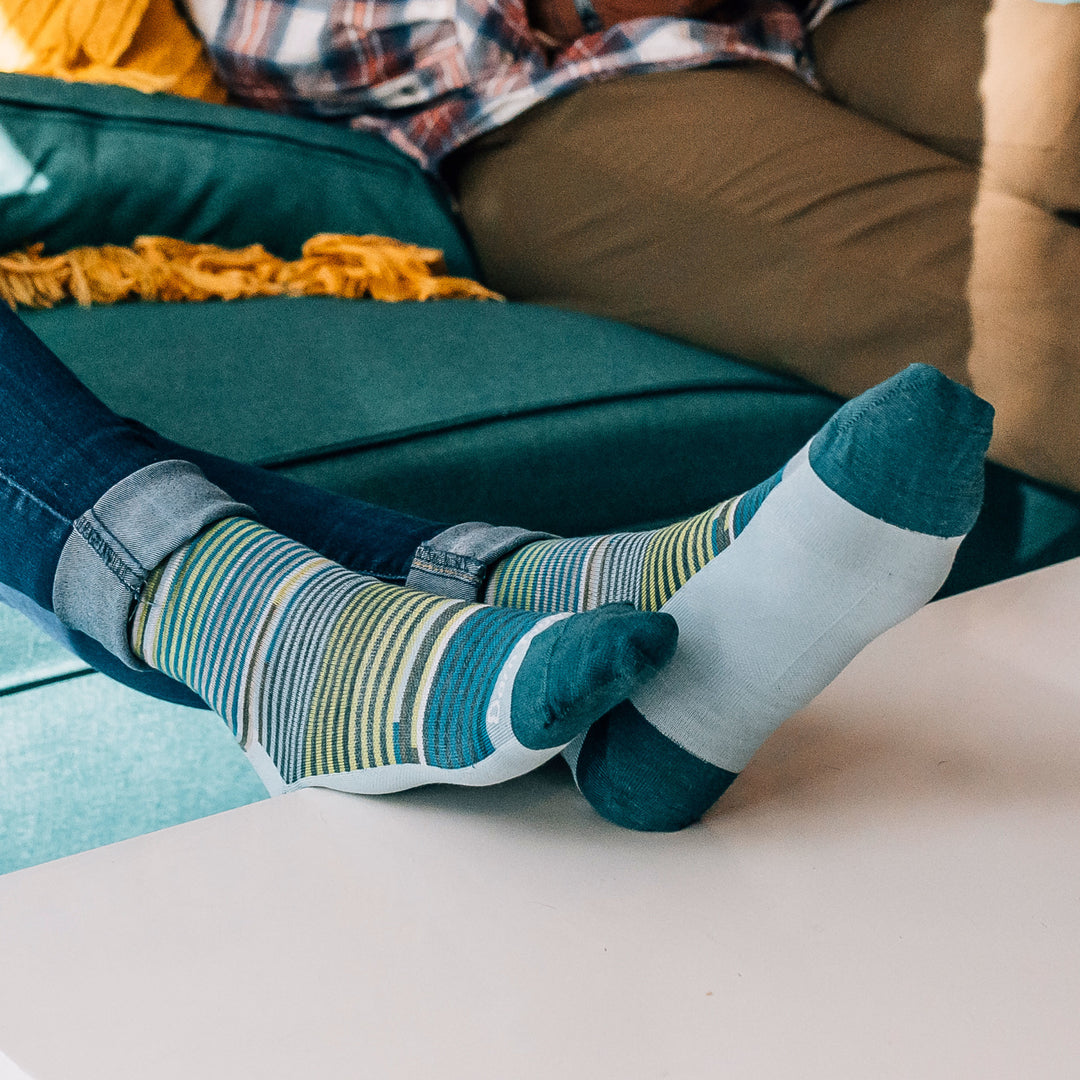 Close up shot of model laying down on a teal couch with her feet up wearing women's pixie crew lifestyle sock in teal
