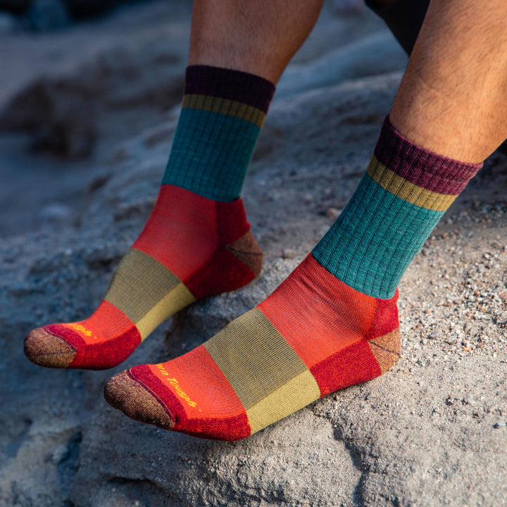 Close up side shot of model sitting on rock wearing men's heady stripe micro crew hiking sock in teal