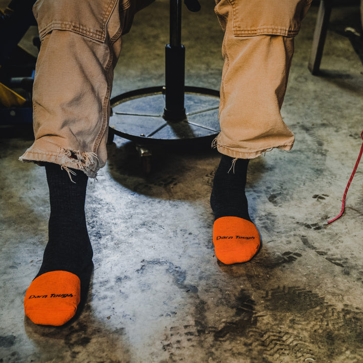 Close up shot of model sitting on shop stool and wearing 2007 socks in Graphite colorway with no shoes 