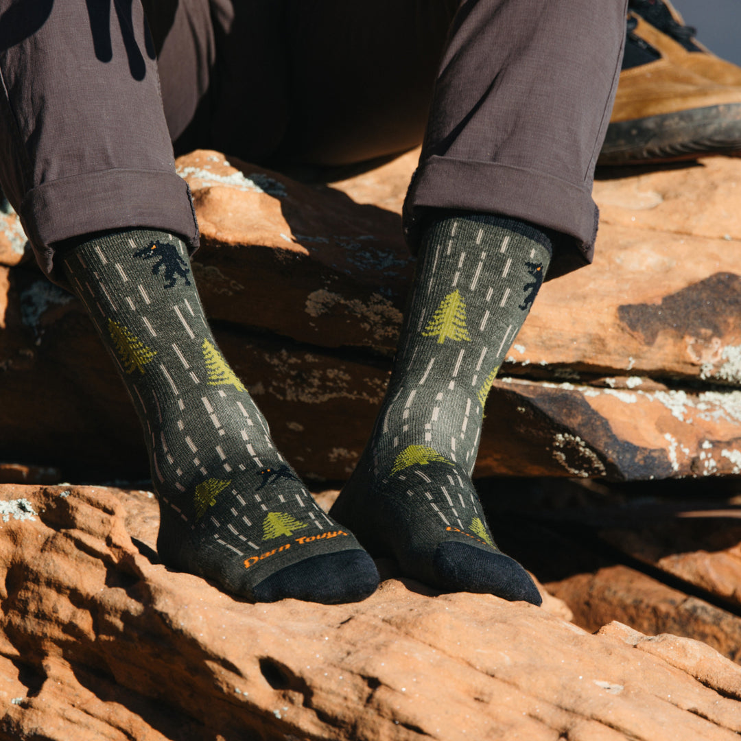 Model in black pants wearing 5015 socks in Forest colorway without wearing shoes against red desert rock