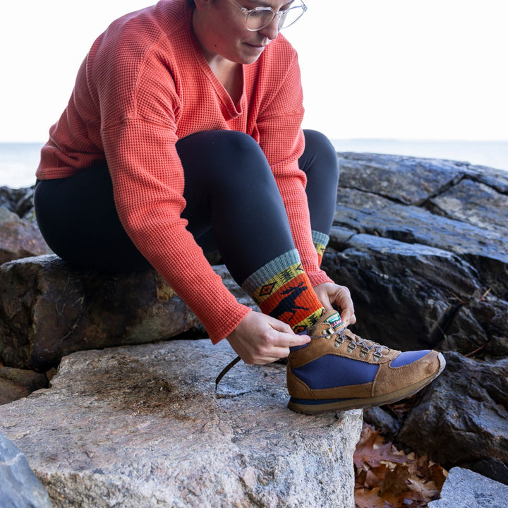 model sitting on rocks tying hiking boot laces wearing 5017 boot midweight with cushion moose meadow sock
