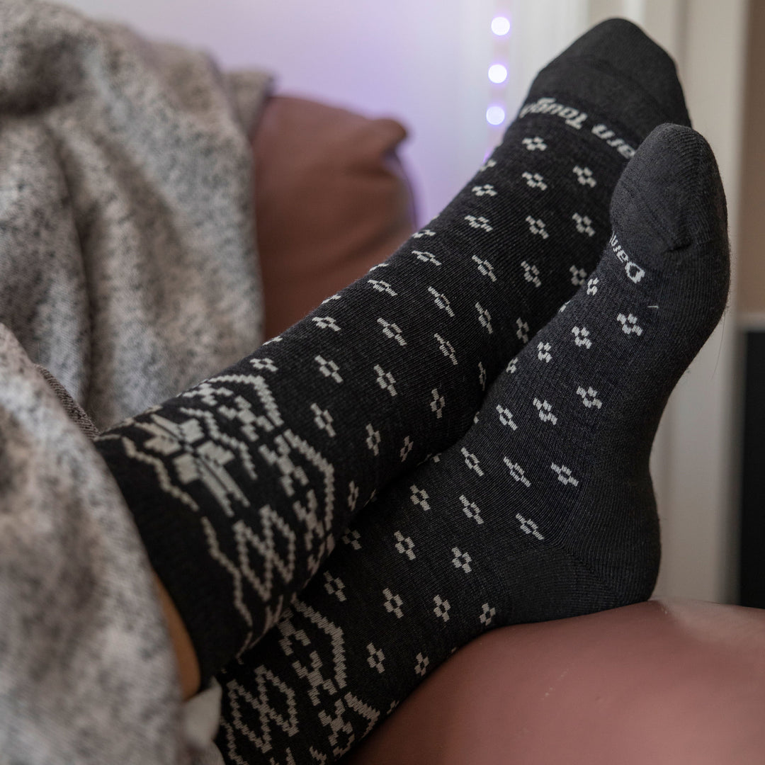 Shot of model laying down on a couch with a gray blanket wearing women's shetland crew lifestyle sock in charcoal