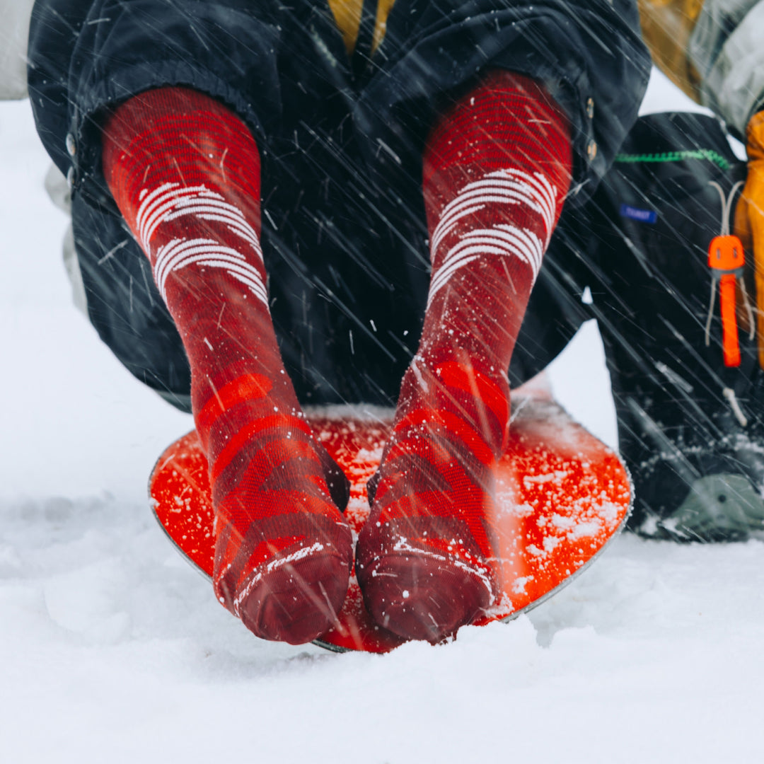 model sitting on snowboard wearing the 8002 pennant RFL over the calf ski and snowboard sock in burgundy colorway 