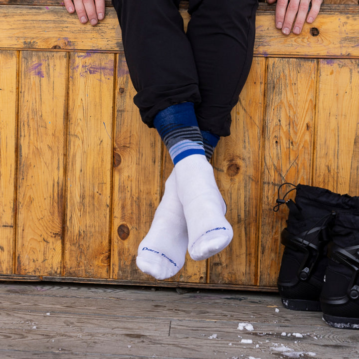 close up of models legs hanging off bench with pant leg rolled up showing 8032 nordic boot lightweight sock in white