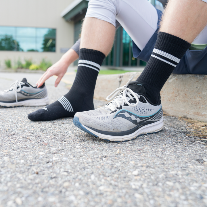Model sitting on curb with one shoe on wearing the 1118 Black element running sock