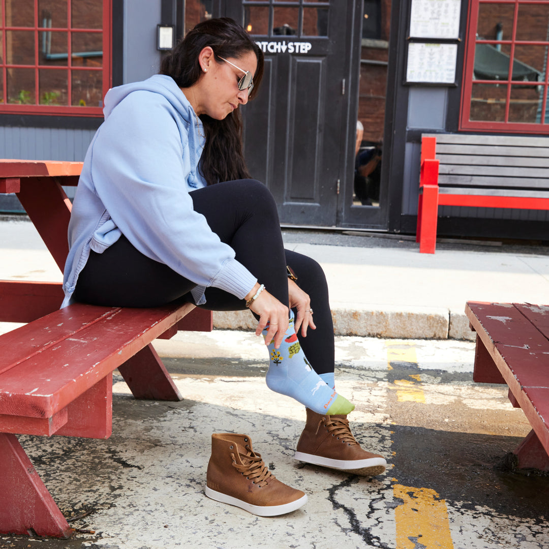Close up on model image pulling up sock wearing the 6054 Sky while sitting on picnic table