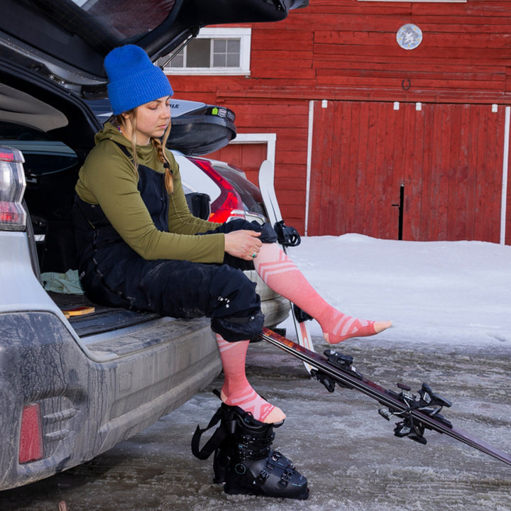 model sitting on edge of car trunk with skis and ski boots putting on 8035 peaks RLF OTC ultra lightweight ski and snowboard sock in canyon