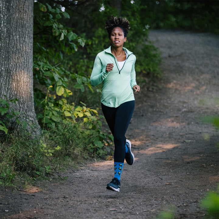 Full shot of model running down a paved pathway wearing the women's toco loco micro crew running socks in baltic blue