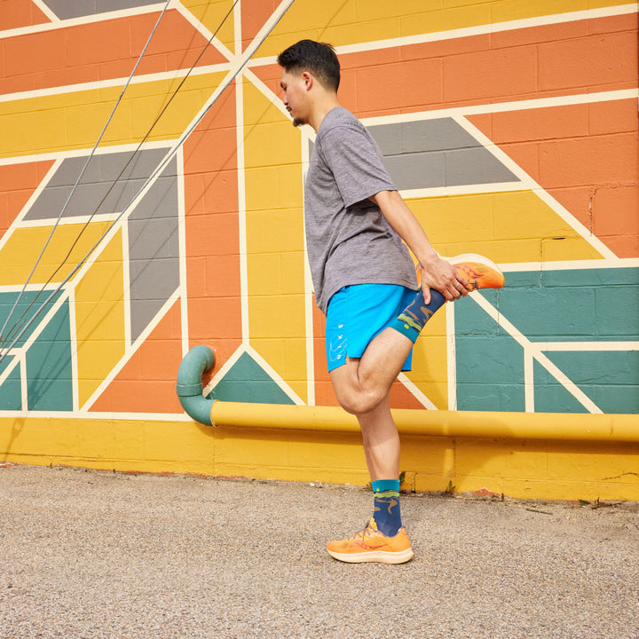 Model standing holding one ankle stretching wearing the 1065 Ridge runner micro crew running sock in Midnight
