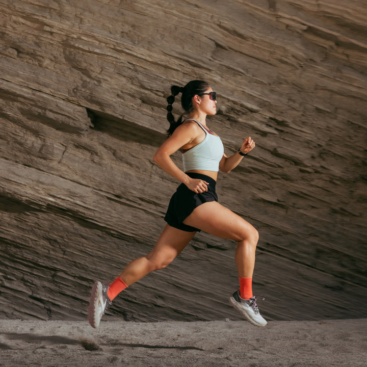 Model running next to rock ledge wearing the 1068 micro crew running sock in coral colorway