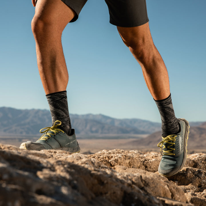 Shot of model on a mountain wearing men's light hiker micro crew hiking sock in space gray with gray hiking shoes