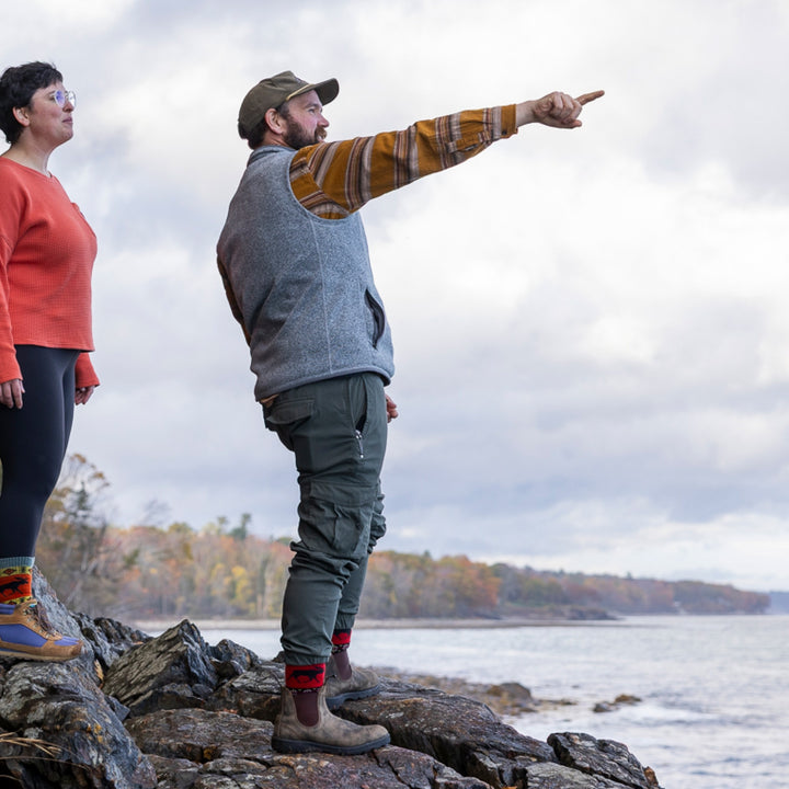 man standing on rocks pointing out to ocean wearing 1980 boot midweight with cushion moose black sock