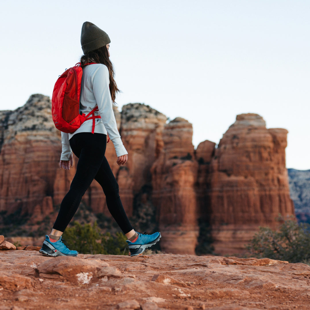model hiking across red desert rock with mountains in background wearing 1986 socks in canyon colorway and blue hiking shoes