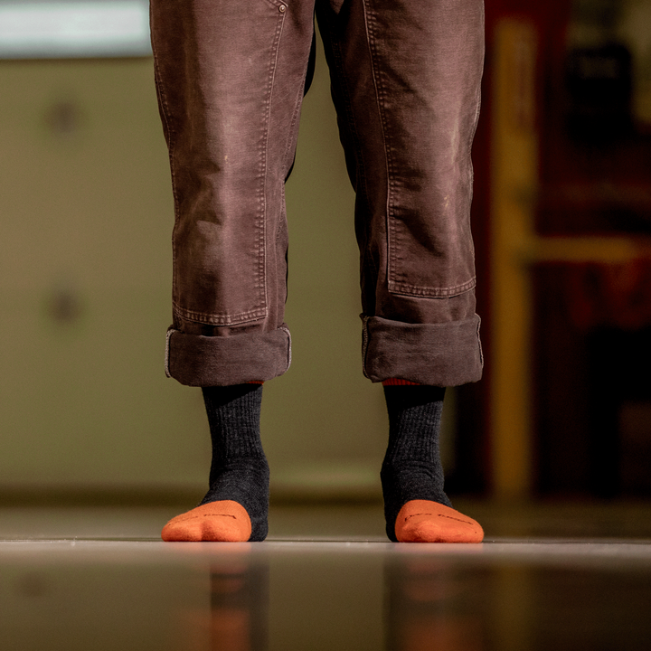 Worker in work pants showing men's steely micro crew socks in graphite black and orange