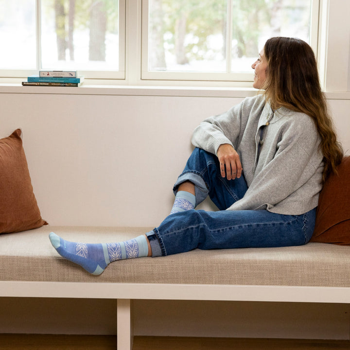 woman sitting on window bench looking out window smiling wearing 6129 elsa crew lightweight with cushion vapor blue sock