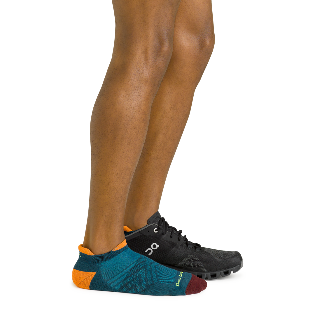Side shot of model wearing the men's no show tab running sock in dark teal with a black sneaker on his left foot