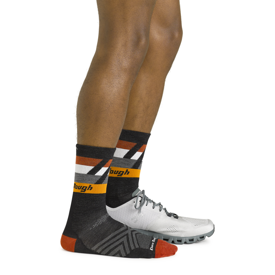 Side shot of model wearing the men's grit micro crew running socks in black with a white sneaker on his left foot