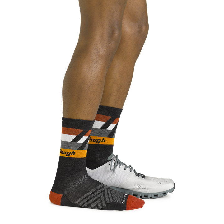 Side shot of model wearing the men's grit micro crew running socks in black with a white sneaker on his left foot