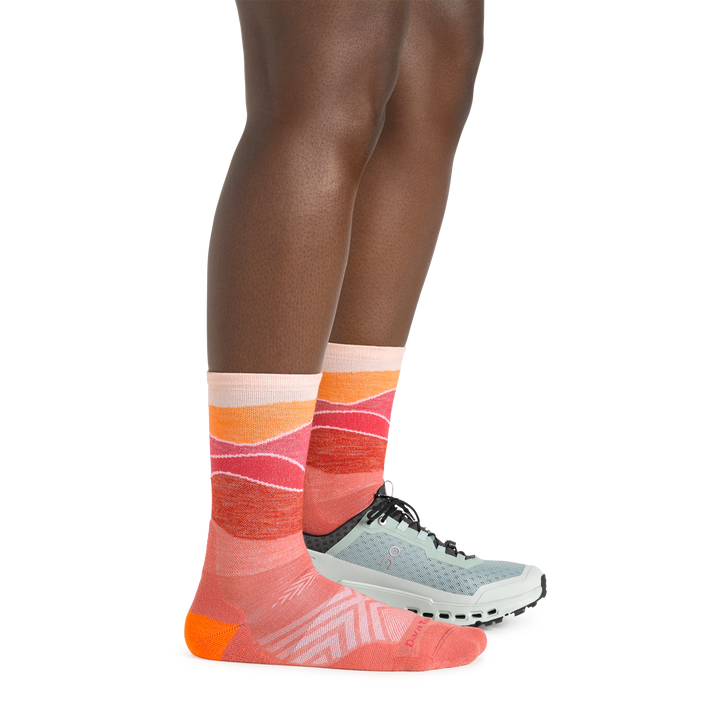 Side shot of model wearing the women's horizon micro crew running sock in canyon pink with a blue shoe on her left foot