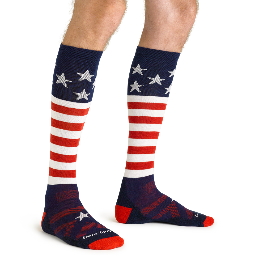 Model standing barefoot wearing Captain Stripe Over the Calf Ski & Snowboard Socks in Stars and Stripes pattern