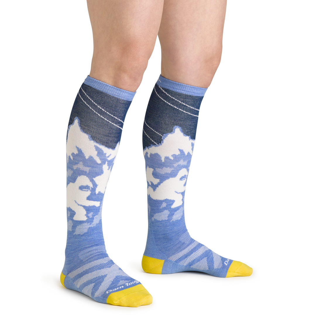 Close up studio shot of model wearing women's yeti over-the-calf midweight ski & snowboard sock in midnight blue