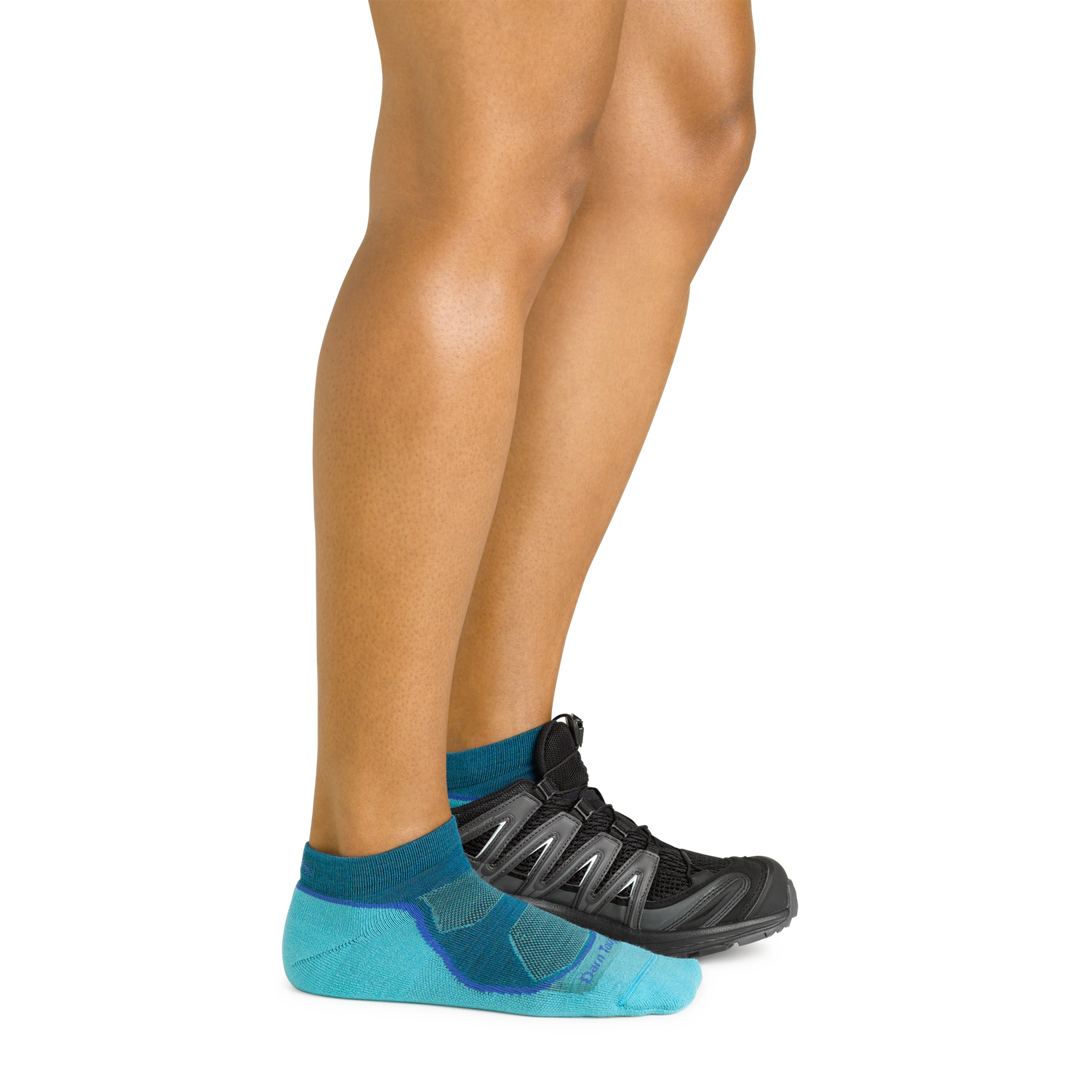 Model wearing the women's light hiker no show hiking sock iin cascade blue with a black shoe on her left foot