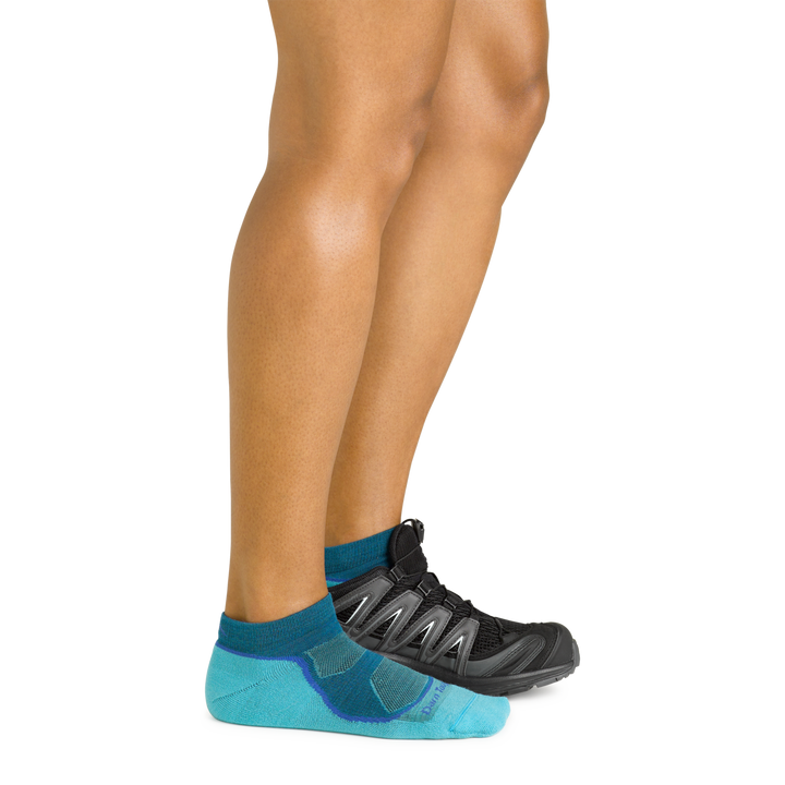 Model wearing the women's light hiker no show hiking sock iin cascade blue with a black shoe on her left foot