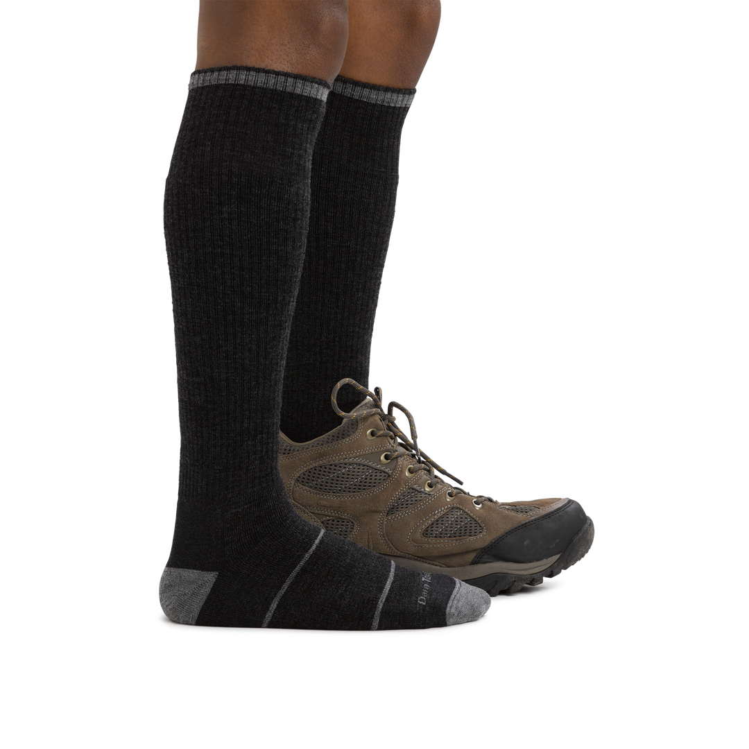 Man standing barefoot wearing Paul Bunyan Over the Calf Midweight Work Sock in Gravel with back foot wearing a boot