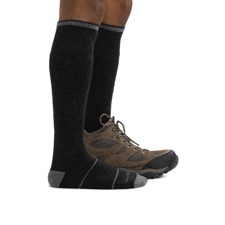 Man standing barefoot wearing Paul Bunyan Over the Calf Midweight Work Sock in Gravel with back foot wearing a boot