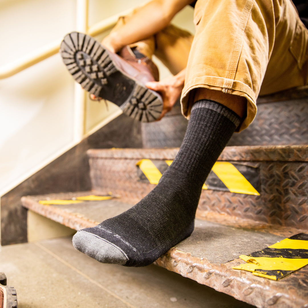 Close up shot of model sitting on steps putting on work boots wearing the men's fred tuttle micro crew work sock in gravel