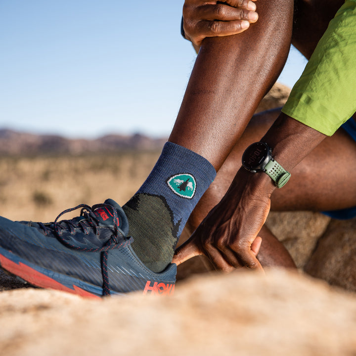 Close up shot of a model sitting in Joshua Tree putting on their shoes while wearing the PCT micro crew hiking sock in forest