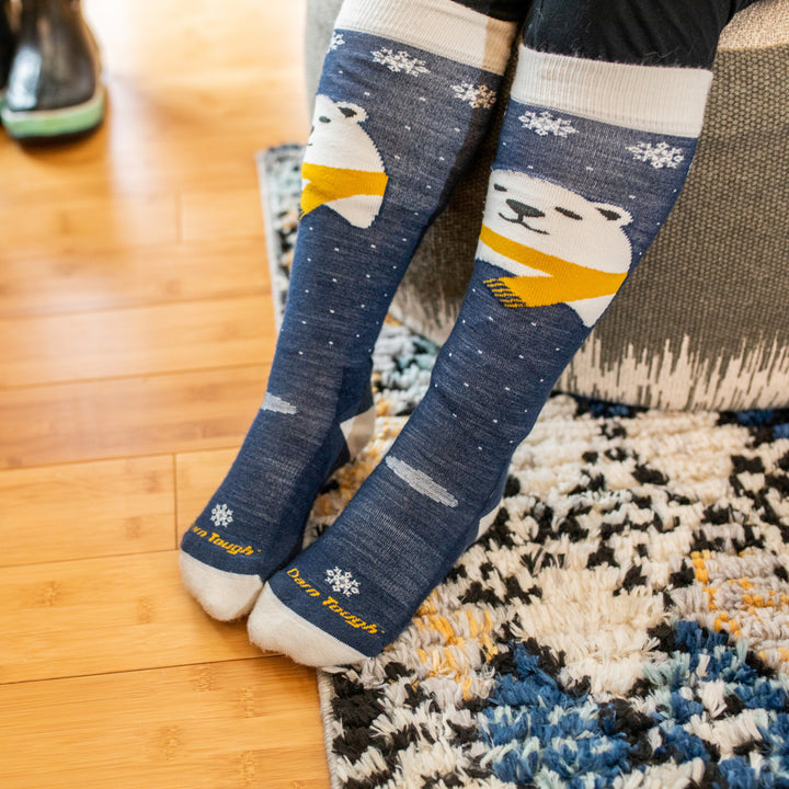 Close up shot of kid wearing Polar Bear socks while sitting on ottoman on top of a rug.