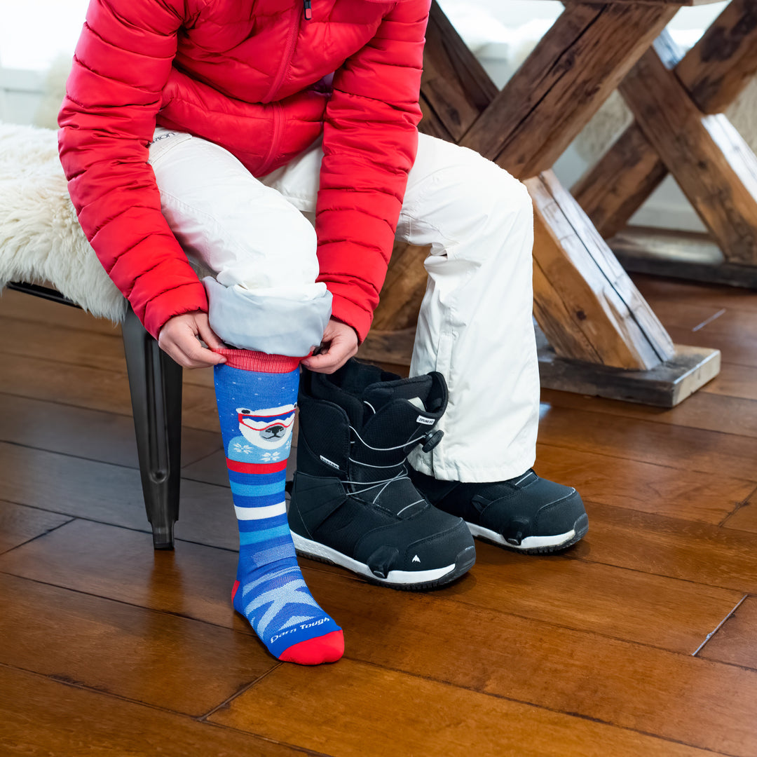 Close up shot of kid sitting on bench while putting on his snowboarding boots, wearing Polar Patroller socks.