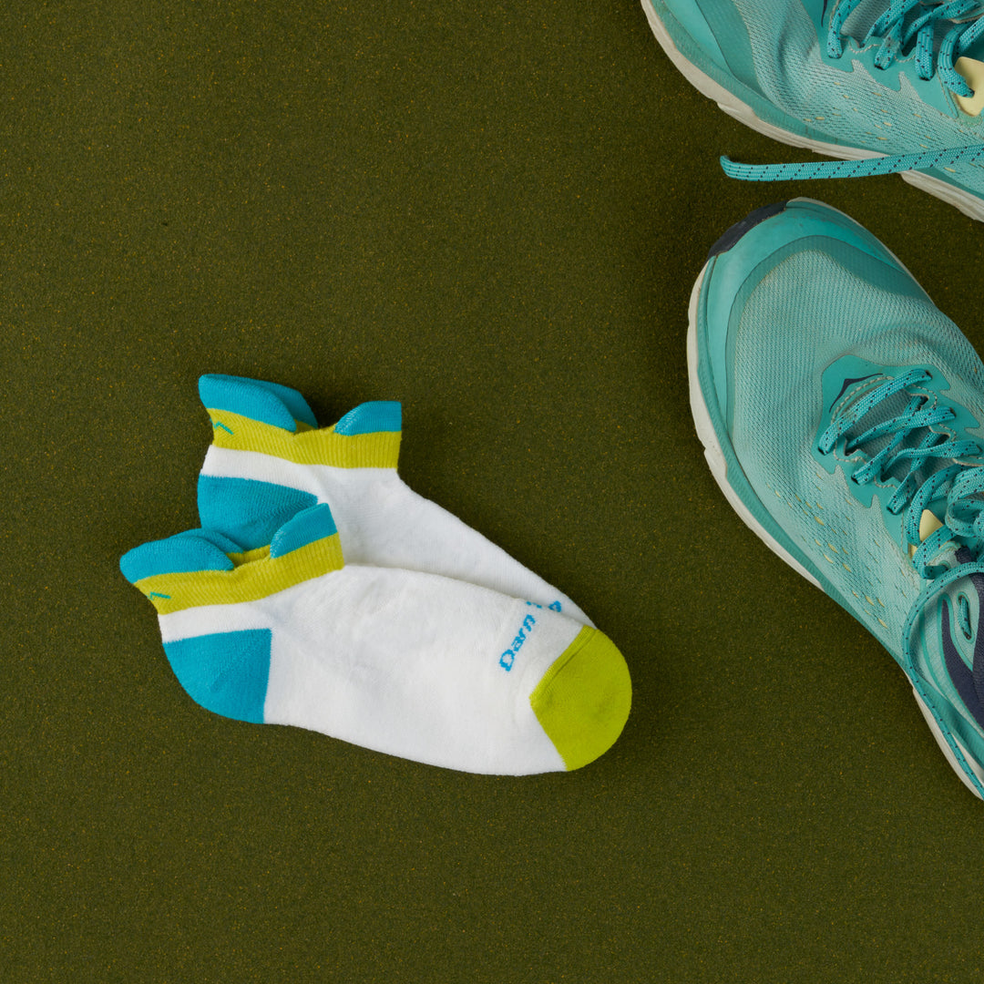 Women's Ultra light no show running sock in white teal laying next to sneakers on green background