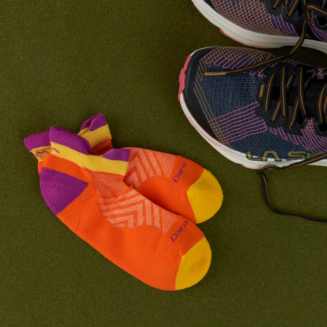 Pair of Ultra lightweight no show running socks in tangerine laying next to sneakers on a green background