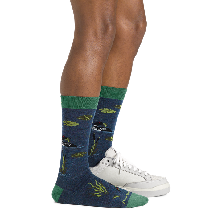 Side studio shot of model wearing men's diver crew lifestyle sock in denim with one white shoe on left foot