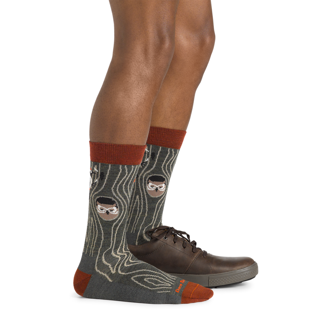 Side studio shot of model wearing men's woody crew lifestyle sock in forest with one brown shoe on left foot
