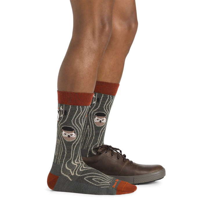 Side studio shot of model wearing men's woody crew lifestyle sock in forest with one brown shoe on left foot