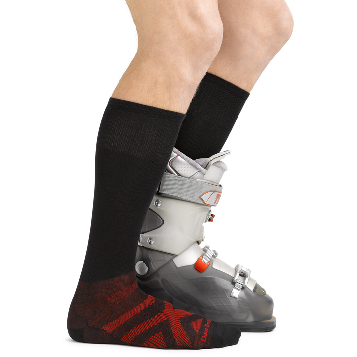 Model wearing the men's thermolite over-the-calfsnow sock in black with a white snow boot on  his left foot
