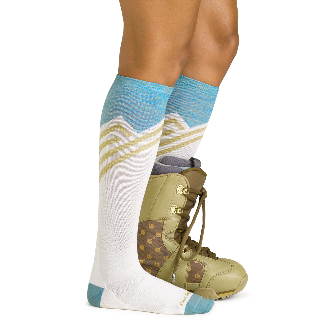 Model wearing women's peaks ove-the-calf lightweight snow sock in white with green snow boot on left foot