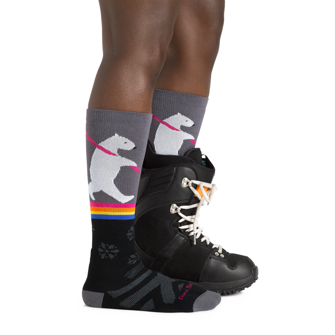 Profile image of a woman's legs facing to the right, wearing Women's Due North Over the Calf Midweight Ski and Snowboard Socks in Black and a ski boot on one foot