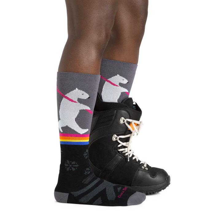 Profile image of a woman's legs facing to the right, wearing Women's Due North Over the Calf Midweight Ski and Snowboard Socks in Black and a ski boot on one foot