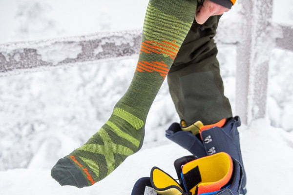 Snowboarder pulling on green ultralight ski socks from darn tough