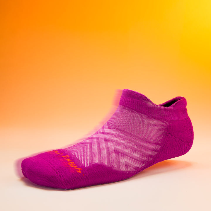 studio shot of womens 1047 Run No Show Tab Ultra-Lightweight with Cushion in clover with orange darn tough text on toe and orange background