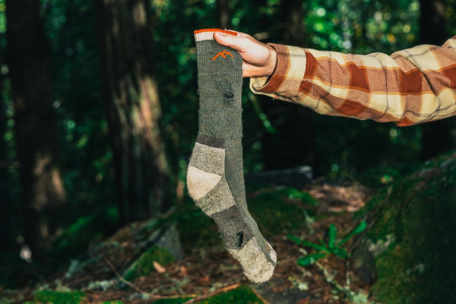 A hand holding up a Darn Tough socks showing serious signs of wear and tear